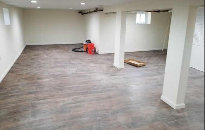 Empty basement room with wood-look flooring, white support columns, and a red equipment case in the corner