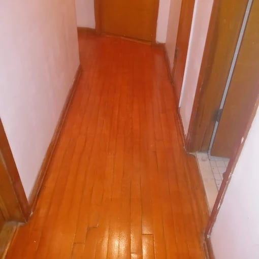 Long narrow hallway with shiny wooden floor and light pink walls with brown doors