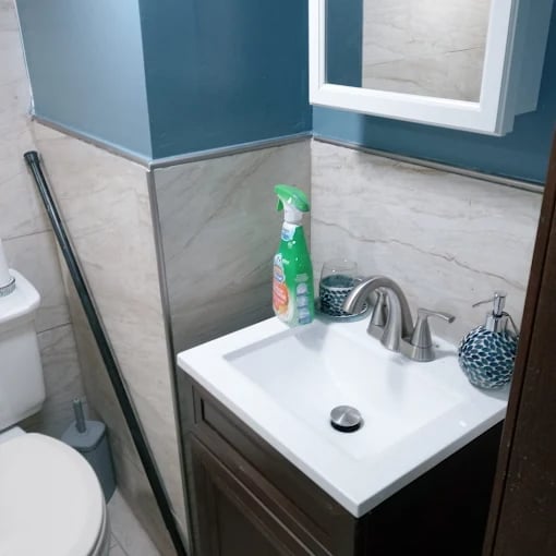 Modern bathroom sink with white countertop, dark vanity, faucet, green bottle, and teal tile wall