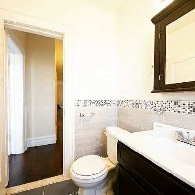 Modern bathroom with white sink, dark vanity, and white toilet against tile backsplash wall