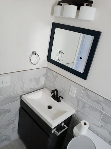 Modern bathroom sink with black vanity, white rectangular basin, black-framed mirror, white subway tile backsplash, and wall-mounted accessories