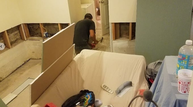 A person working on bathroom renovation with drywall sheets installed and tools scattered around the space