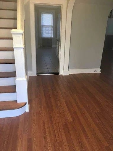 Entry hallway with wooden flooring, white trim, glass door leading outside, and staircase on left